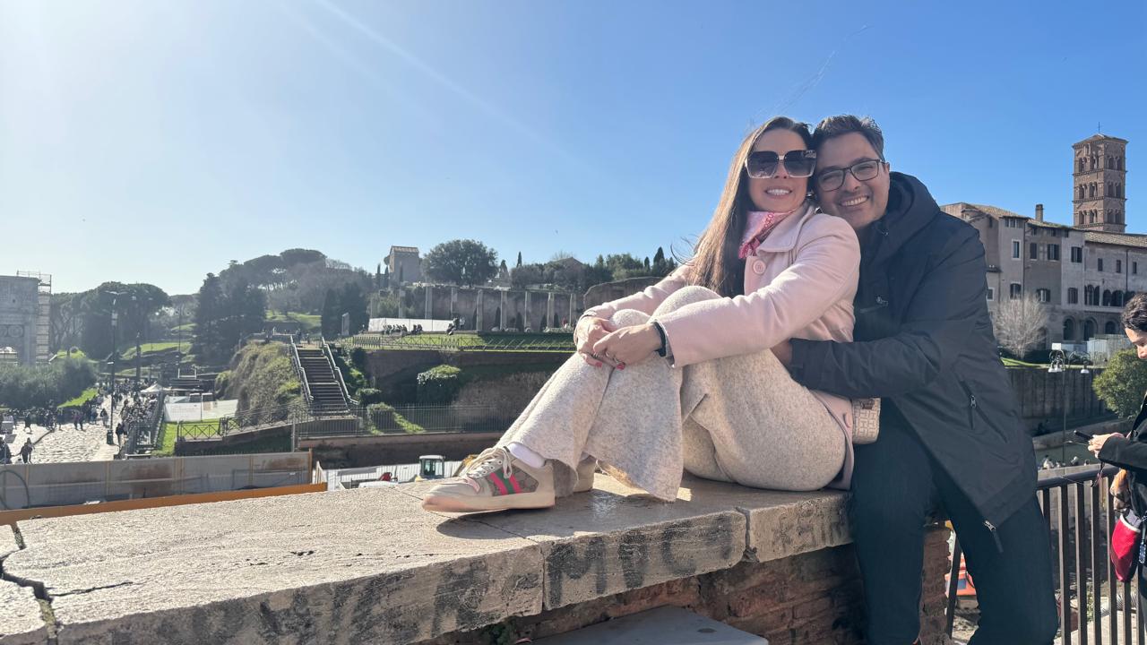 O casal abraçado em uma mureta com vista para o Fórum Romano